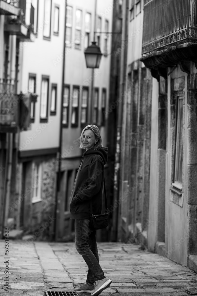 A woman in a hoodie walks through an old Portuguese town. Black and white photo.