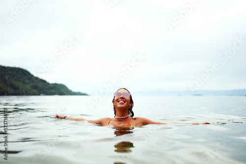 woman standing shoulder deep in water with arms open eyes closed smiling happy
