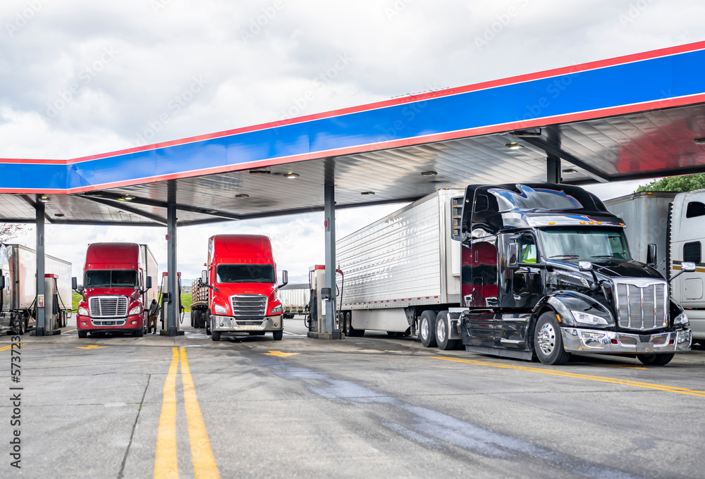 Fototapeta premium Long haulers big rigs semi trucks with semi trailers fuel tanks with diesel standing on the gas station on the truck stop
