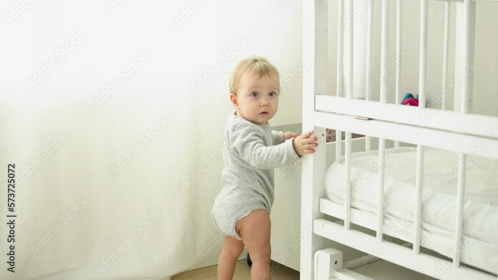 Baby taking first steps near the bed. Little girl learning to walk Baby taking first steps near the bed. Little girl learning to walk