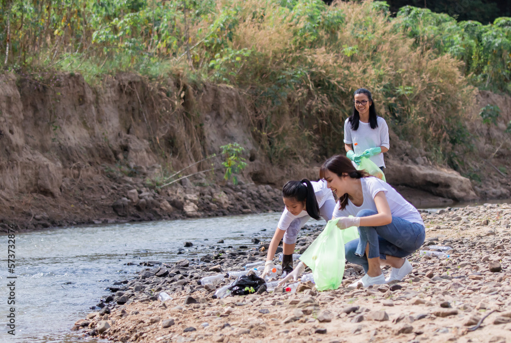 Disposal recycling and waste management concept, group of Asian friends collect dirty plastic bottles in the stream for recycle, volunteer family pick up garbage and wastrel that tourist throw in park