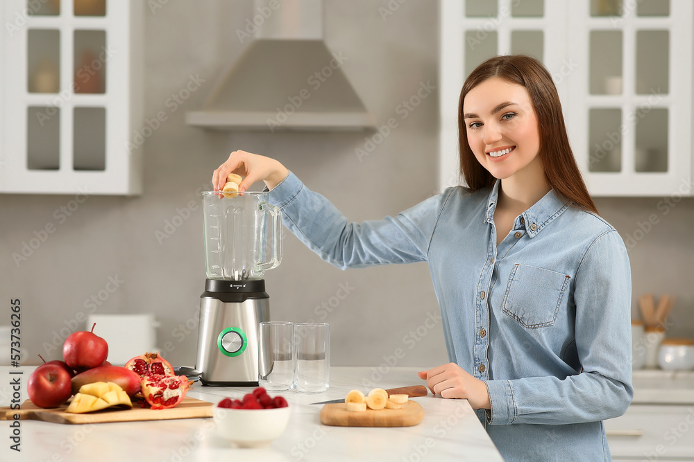 Beautiful young woman adding banana into blender for tasty smoothie in kitchen Beautiful young woman adding banana into blender for tasty smoothie in kitchen