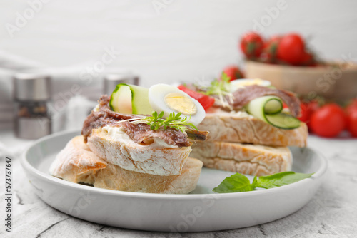 Delicious bruschettas with anchovies, tomato, cucumber, egg and cream cheese on white textured table, closeup