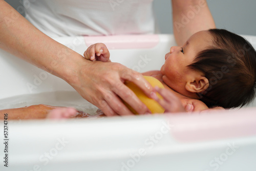 mother give a bath newborn baby in bathtub