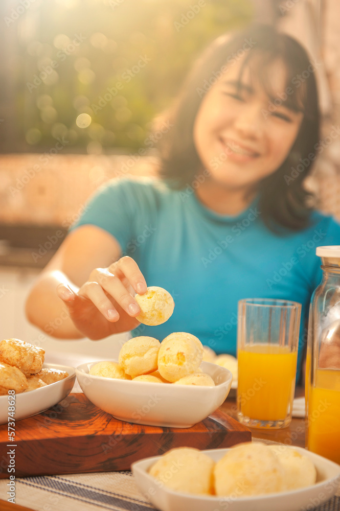 Young woman picking up a chesse bread on the serving dish. Focus on the cheese bread. (Pao de queijo) Young woman picking up a chesse bread on the serving dish. Focus on the cheese bread. (Pao de queijo)