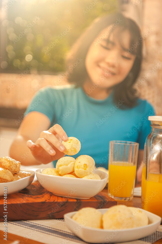 Young woman picking up a chesse bread on the serving dish. Focus on the cheese bread. (Pao de queijo) Young woman picking up a chesse bread on the serving dish. Focus on the cheese bread. (Pao de queijo)