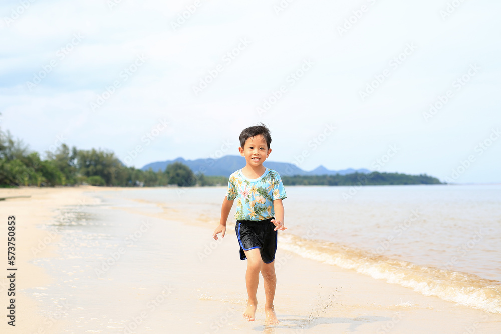 Asian little boy having fun running on tropical sand beach.