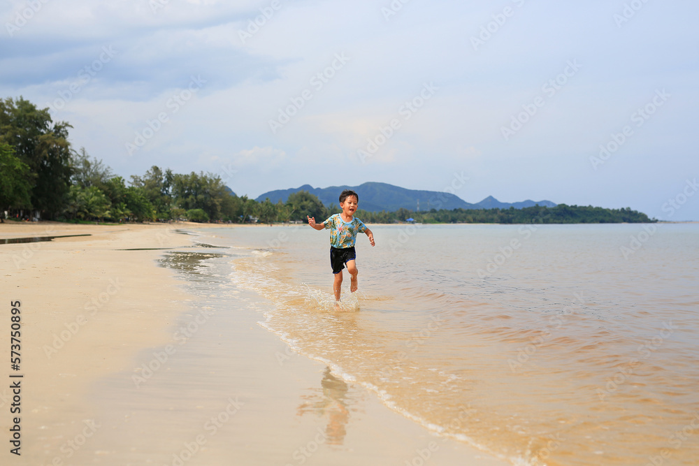 Happy Asian little boy having fun running on tropical sand beach