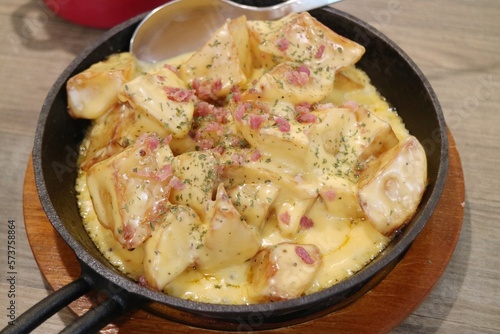 Baked cheese potato cubes and ham slices in an iron plate