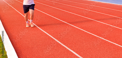 Low section of young man jogging on running track in outdoors stadium, panoramic view with motion blurred