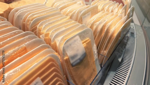 Sliced cheese in Styrofoam containers, wrapped in clingfilm, stands in rows in the supermarket fridge photo