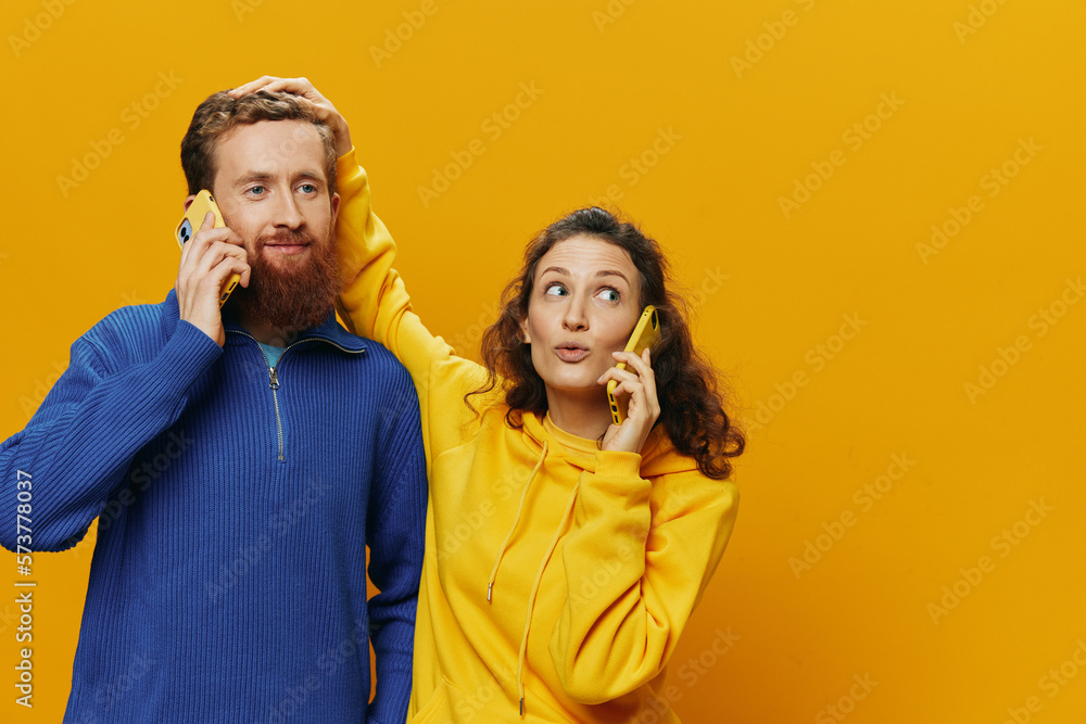 Woman and man cheerful couple with phones in hand talking on cell phone crooked smile cheerful, on yellow background. The concept of real family relationships, talking on the phone, work online. Woman and man cheerful couple with phones in hand talking on cell phone crooked smile cheerful, on yellow background. The concept of real family relationships, talking on the phone, work online.