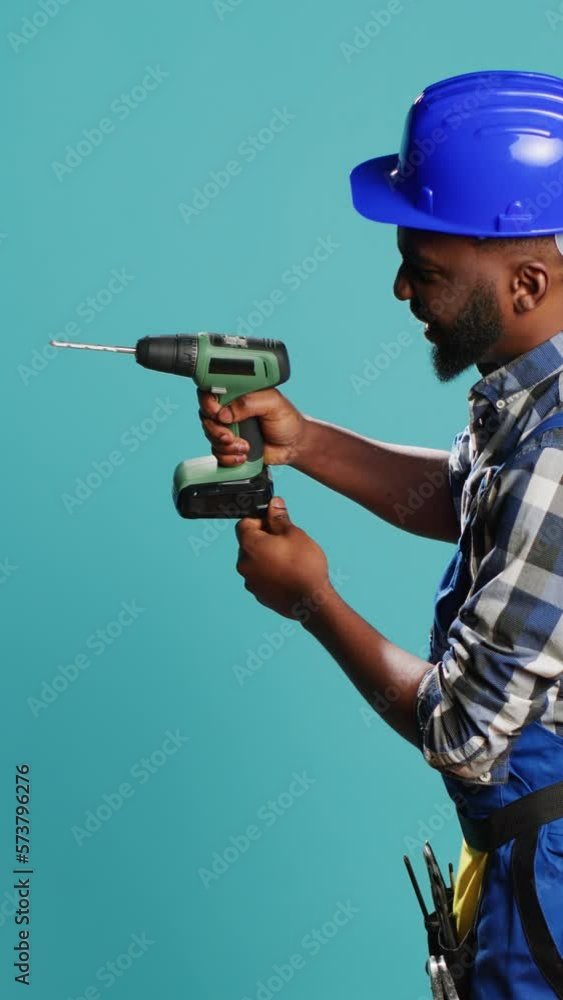 Vertical video: Male builder using power drill instrument on wall, drilling nails with cordless machine tool on camera. Professional mechanic with hardhat holding nail gun to drill holes, building Vertical video: Male builder using power drill instrument on wall, drilling nails with cordless machine tool on camera. Professional mechanic with hardhat holding nail gun to drill holes, building