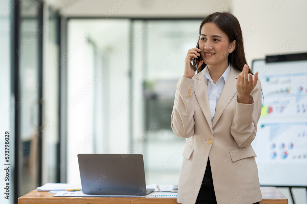 Beautiful asian businesswoman working with laptop computer is using mobile phone for talking. Finance business contacts in real estate projects in her office. Beautiful asian businesswoman working with laptop computer is using mobile phone for talking. Finance business contacts in real estate projects in her office.