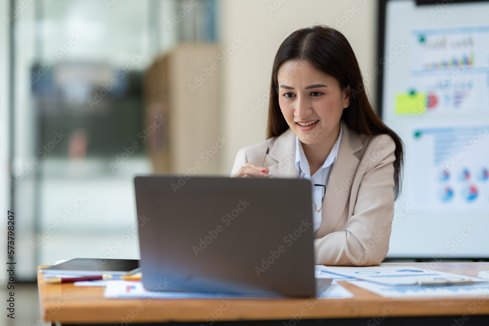 Attractive asian businesswoman holding eyeglasses working with financial, management, marketing data from laptop computer showing revenue data in growing real estate projects. Attractive asian businesswoman holding eyeglasses working with financial, management, marketing data from laptop computer showing revenue data in growing real estate projects.