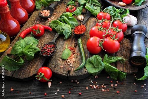 Fresh, red, ripe tomatoes on a wooden table, decorated with fresh basil leaves, spices, hot peppers, garlic, tomato juice and olive oil.
