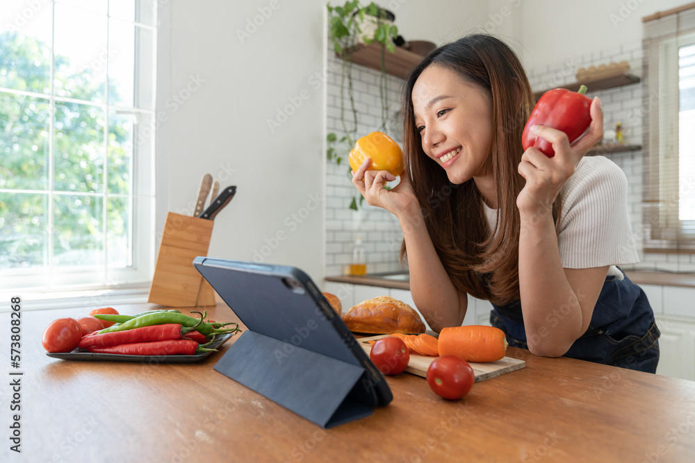 Asian girl in apron learning online, learning, teaching, choosing ingredients for cooking vegetables. happy fruit via tablet lifestyle and healthy cooking concept.