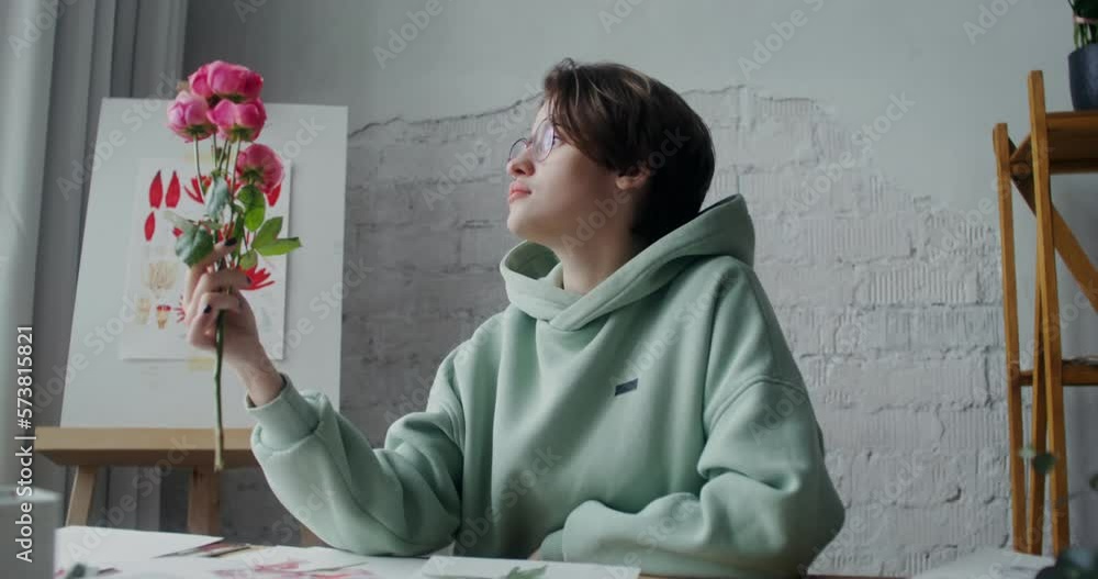 A young female artist admires fresh flowers while looking for inspiration to paint a painting while working in a studio in daylight A young female artist admires fresh flowers while looking for inspiration to paint a painting while working in a studio in daylight