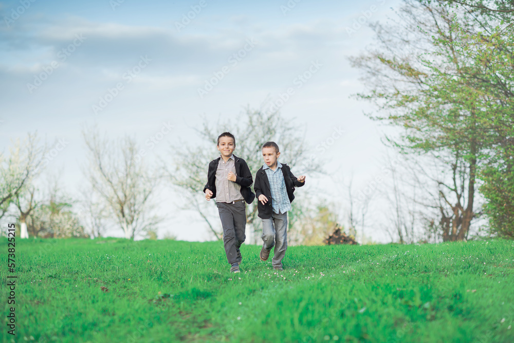 two boys run across the green meadow, looking forward to the spring, the concept of a happy childhood two boys run across the green meadow, looking forward to the spring, the concept of a happy childhood