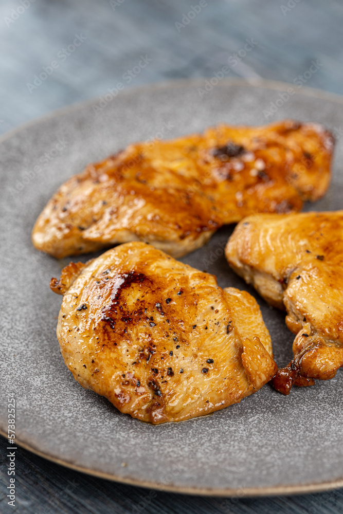 Chicken breasts barbecued and served on the blue plate above dark moody background Chicken breasts barbecued and served on the blue plate above dark moody background