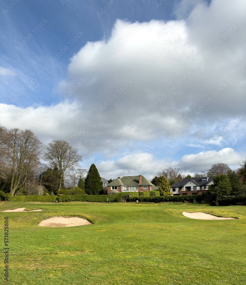 Flag and the hole at golf club The Mere Cheshire, blue sky summers day with some clouds. Large surrounding houses Flag and the hole at golf club The Mere Cheshire, blue sky summers day with some clouds. Large surrounding houses