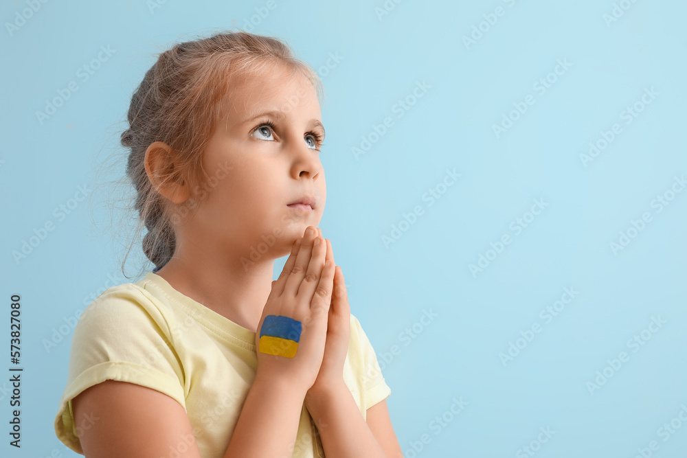 Little girl with drawn flag of Ukraine praying on blue background Little girl with drawn flag of Ukraine praying on blue background
