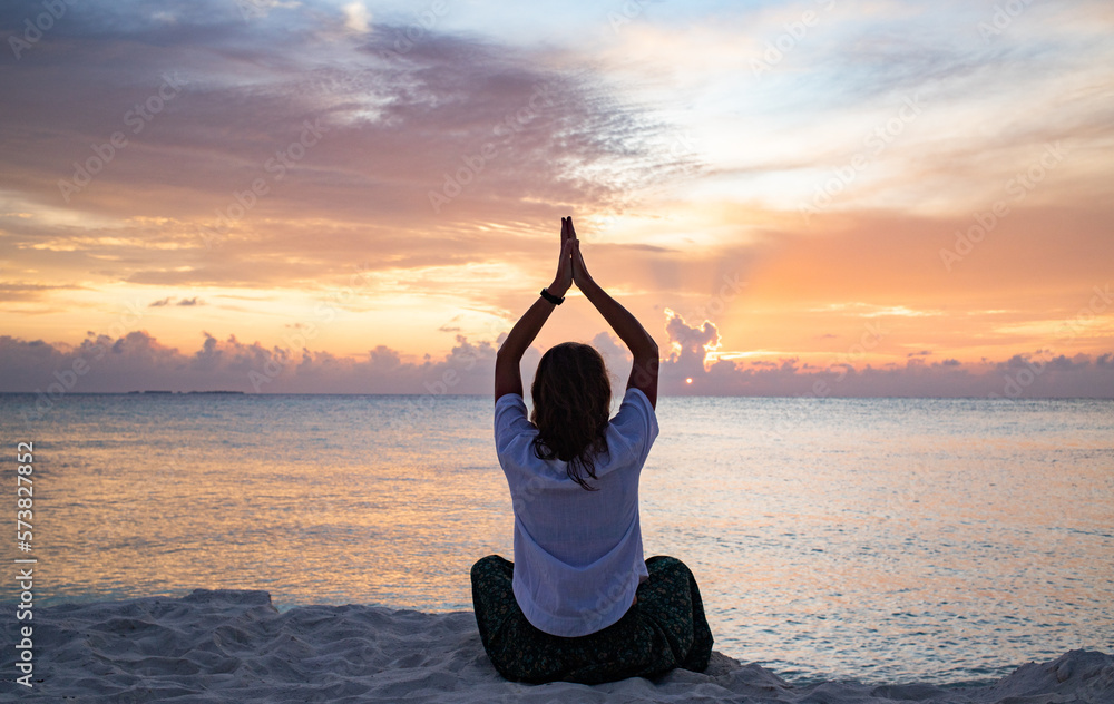 woman doing yoga at sunset on tropical beach