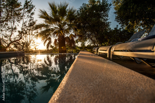 Palm trees backlits by the settling sun reflected in the pool's water. Mallorca, Spain.