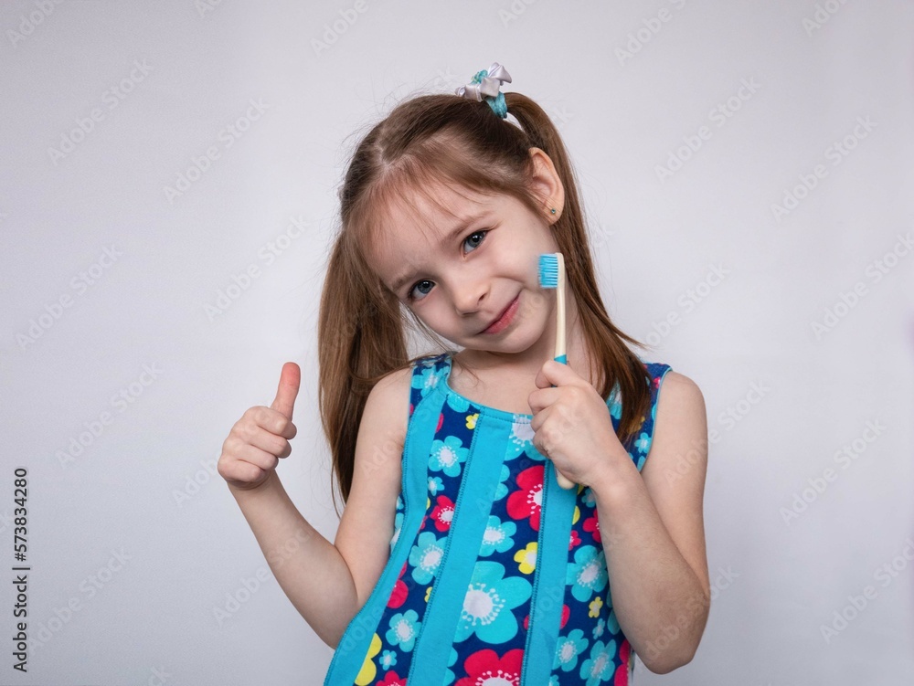 A little girl smiles shyly, holds a toothbrush in her hands and gives a thumbs up. The concept of pediatric dentistry A little girl smiles shyly, holds a toothbrush in her hands and gives a thumbs up. The concept of pediatric dentistry