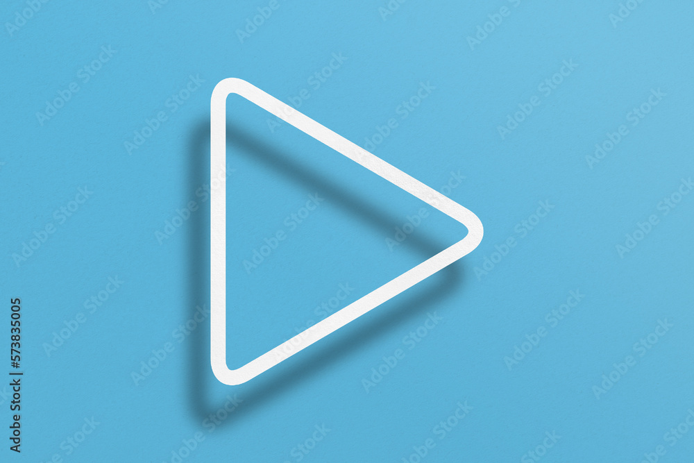 White paper cut into triangle shape, play button set on light blue paper background. White paper cut into triangle shape, play button set on light blue paper background.