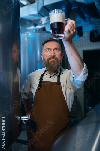 Bearded senior brewer checking beer quality during brewing technology process