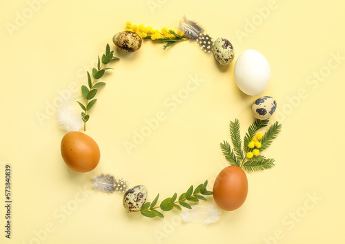 Fototapeta Naklejka Na Ścianę i Meble -  Frame made of Easter eggs, mimosa flowers and eucalyptus branches on yellow background