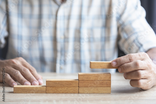 Fototapete Business man's hand is stacking brown wooden block from low to higher