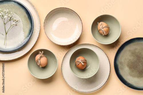 Set of crockery with Easter eggs and gypsophila flowers on beige background