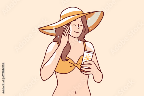 Woman who wants to sunbathe applies sunblock cream to skin to protect herself from sunstroke or to avoid excessive tanning. Girl in bikini and beach hat uses sunblock cream enjoy summer vacation 
