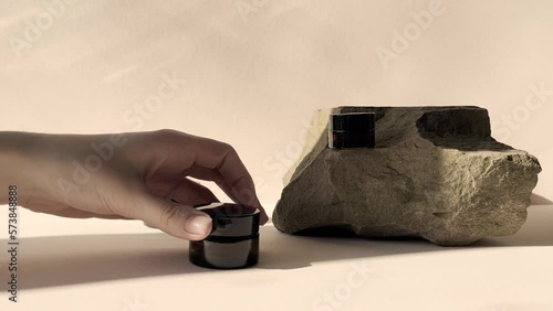 Woman apply beauty product skin care cosmetic spa cream serum in the amber packaging.A hand opens the lid of jar with cream on a beige background in the morning rays of the sun.