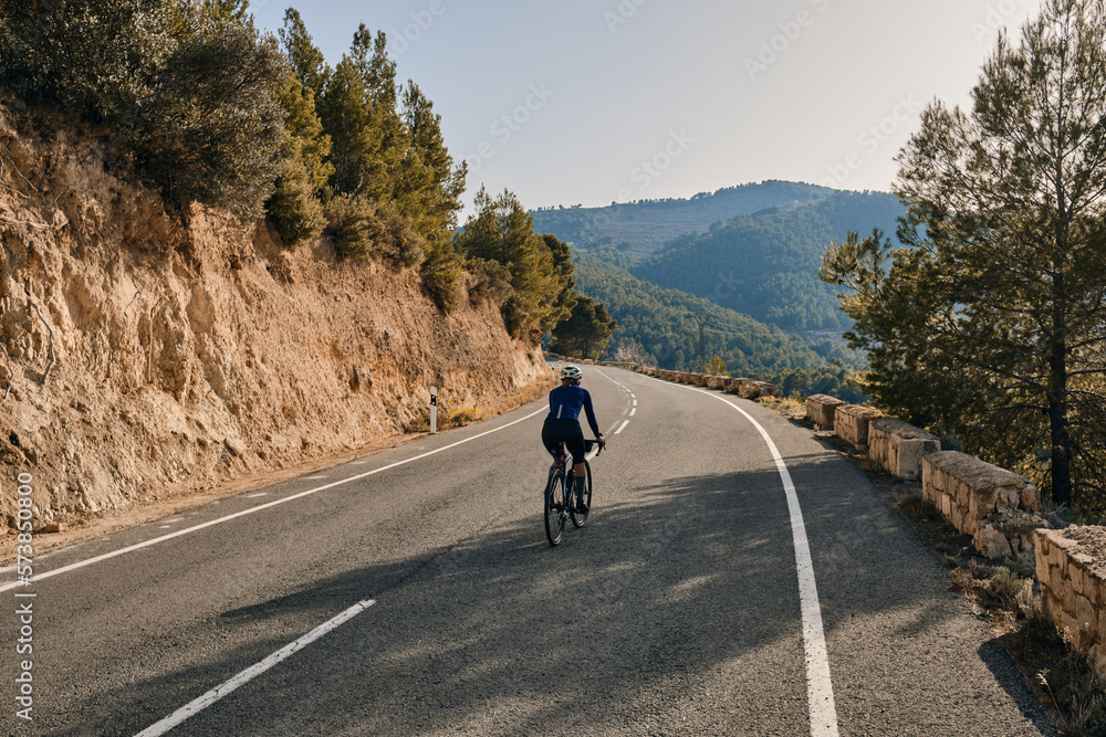 Fit young female cyclist riding on the road on a gravel bike at sunset ...