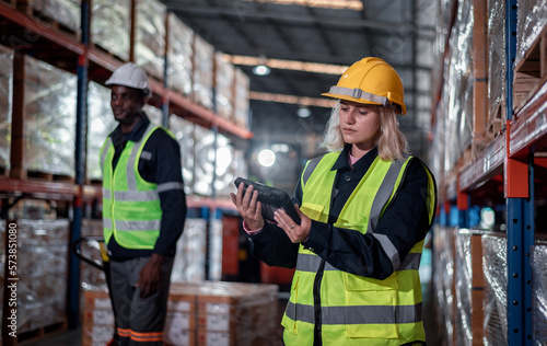 Worker industry warehouse in helmets woman order details and checking goods and supplies on shelves with goods background in warehouse is industry logistic and business export concept.