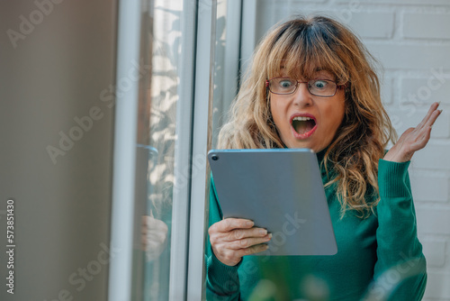 middle aged woman with digital tablet looking surprised