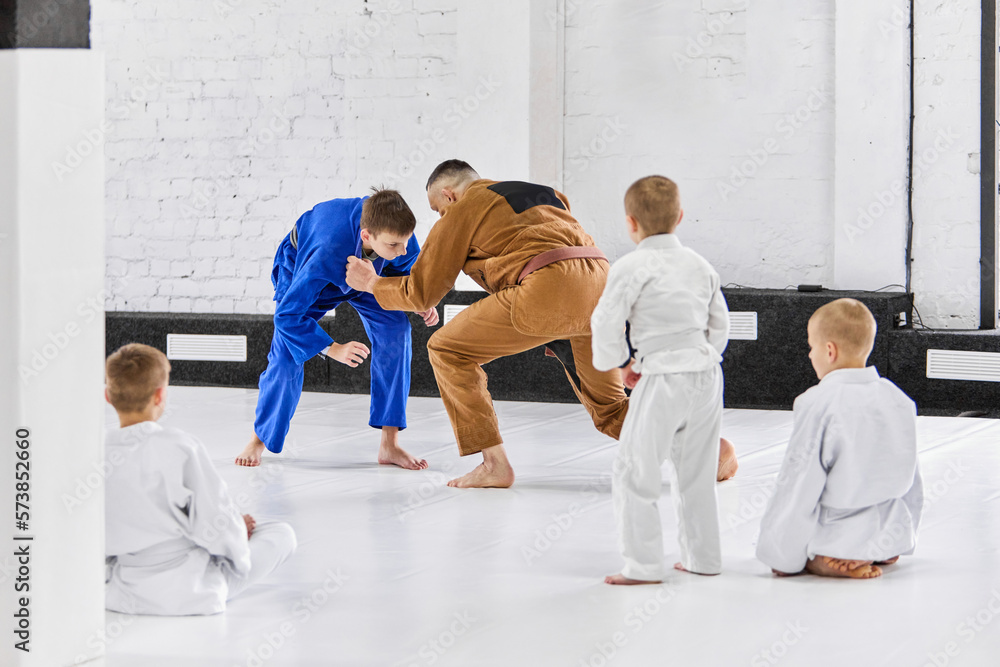 Man, professional sport coach teaching boys, children judo, jiu-jitsu fight activity. Professional athletes and kids. Concept of martial arts, combat sport, sport education, childhood Man, professional sport coach teaching boys, children judo, jiu-jitsu fight activity. Professional athletes and kids. Concept of martial arts, combat sport, sport education, childhood
