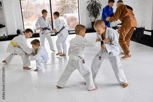 Little boys, children in white kimono training judo, jiu-jitsu sport activity indoors with professional coach. Concept of martial arts, combat sport, sport education, childhood photo