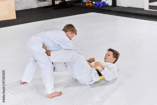 Two boys, children in white kimono training judo, jiu-jitsu fight style indoors. Developing strength and sportive knowledges. Concept of martial arts, combat sport, sport education, childhood,