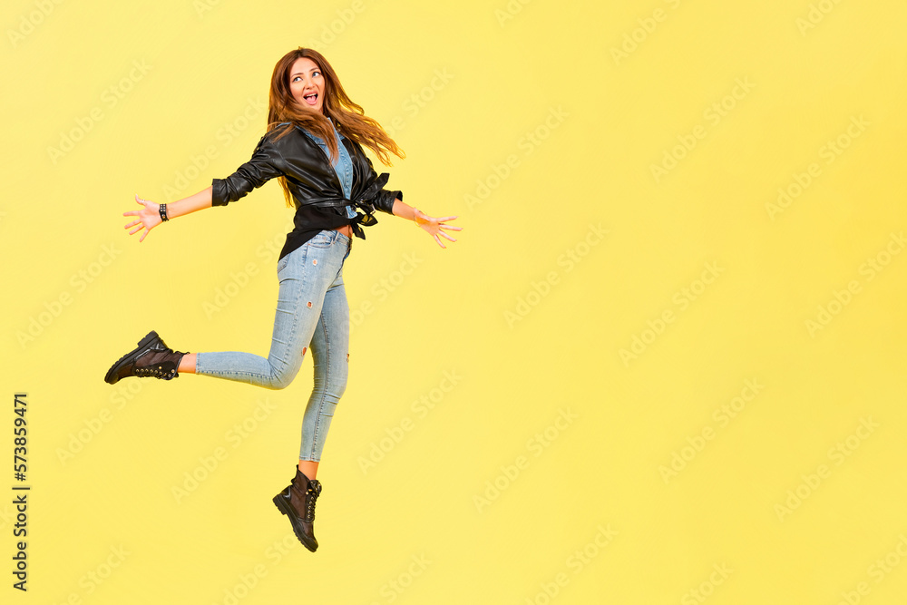 Yellow background, a girl in a leather jacket in the style of rock, shows emotions, free space for text, jumps