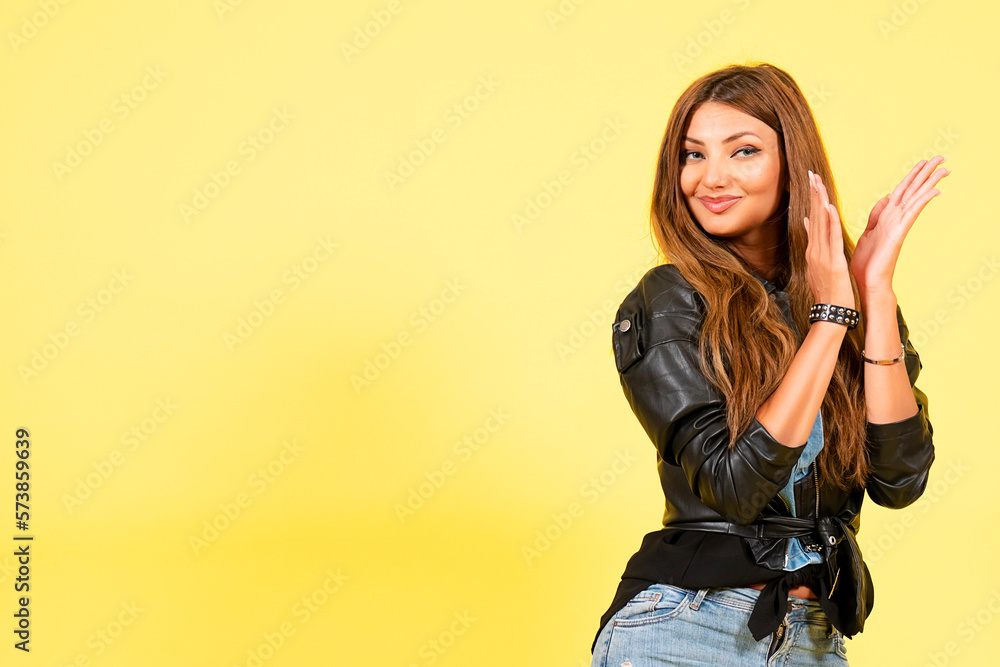 Yellow background, girl in a leather jacket in rock style, shows emotions, free space for text, claps