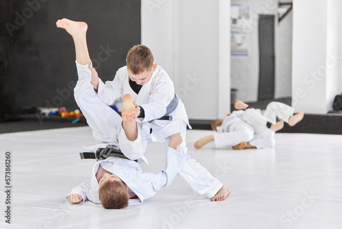 Boys, children in white kimono training, practising judo, jiu-jitsu exercises indoors. Concept of martial arts, combat sport, sport education, childhood, strength, hobby
