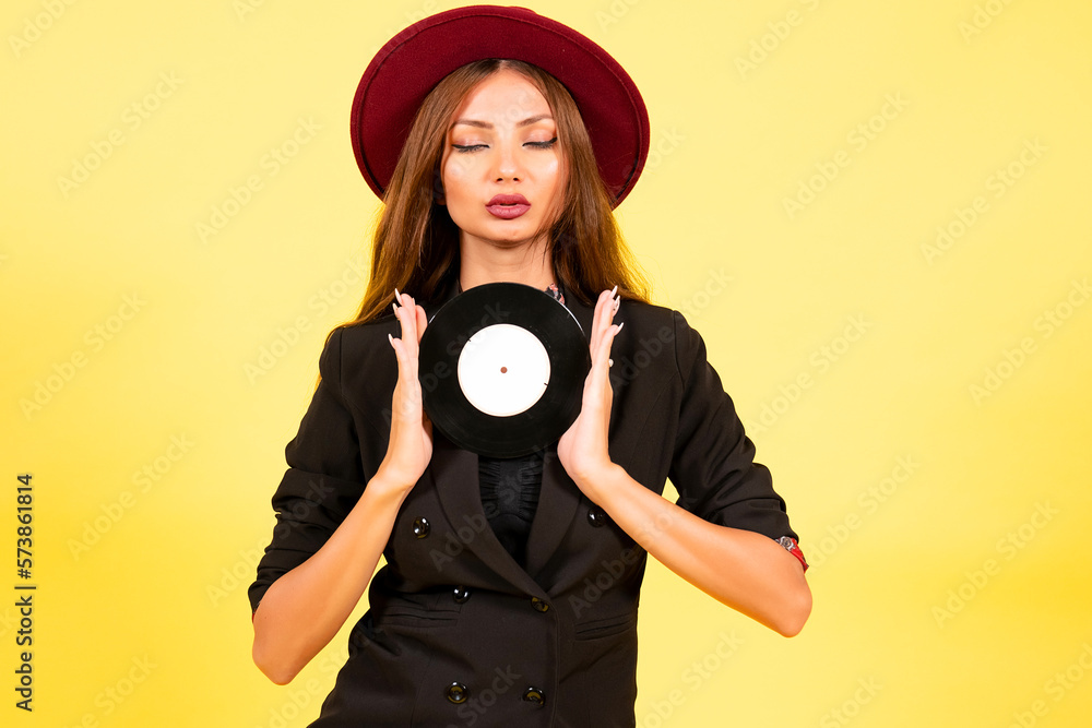 Fototapeta premium girl in a black suit on a yellow background with a record in her hands, music, the girl shows emotions