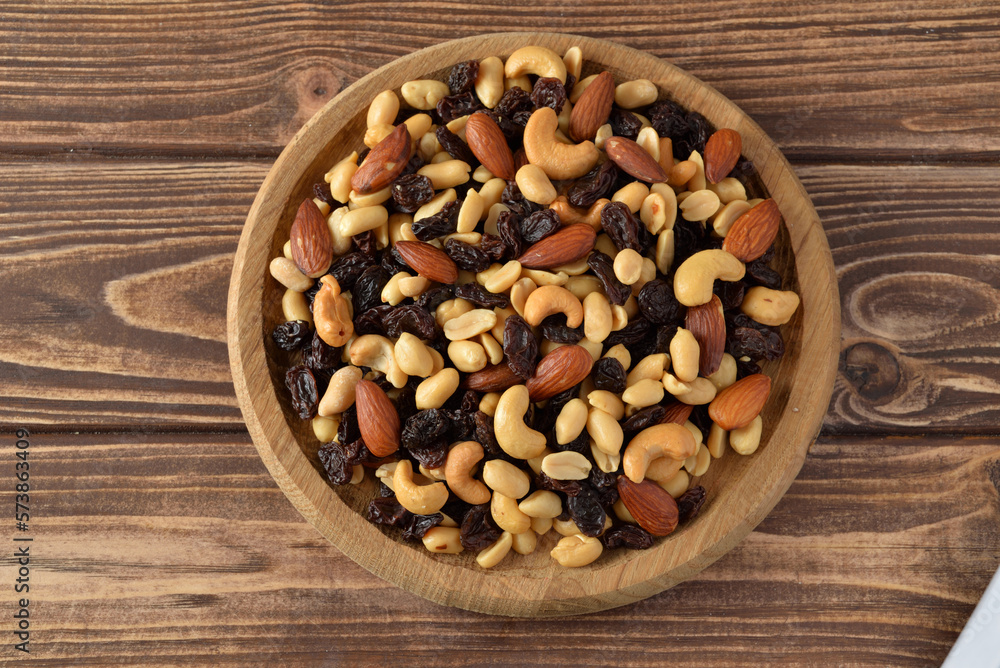 Nuts mixture of almond, cashew, peanut and raisin in wooden plate on wooden table Nuts mixture of almond, cashew, peanut and raisin in wooden plate on wooden table