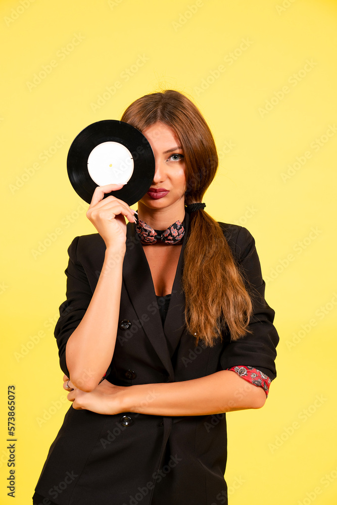 girl in a black suit on a yellow background with a record in her hands, music, the girl shows emotions girl in a black suit on a yellow background with a record in her hands, music, the girl shows emotions
