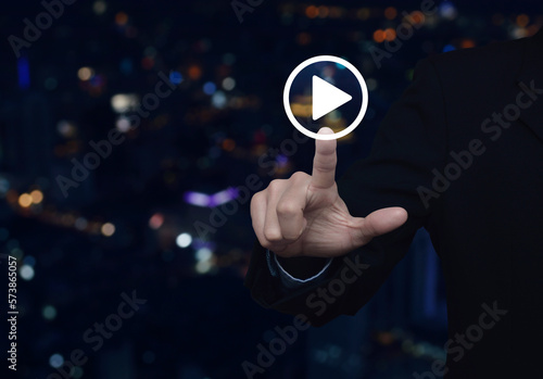 Businessman pressing play button icon over blur colorful night light city tower and skyscraper, Business music online concept