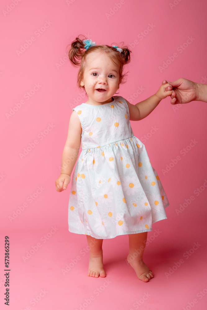 a baby girl stands on a pink background holding her mother's hand a baby girl stands on a pink background holding her mother's hand